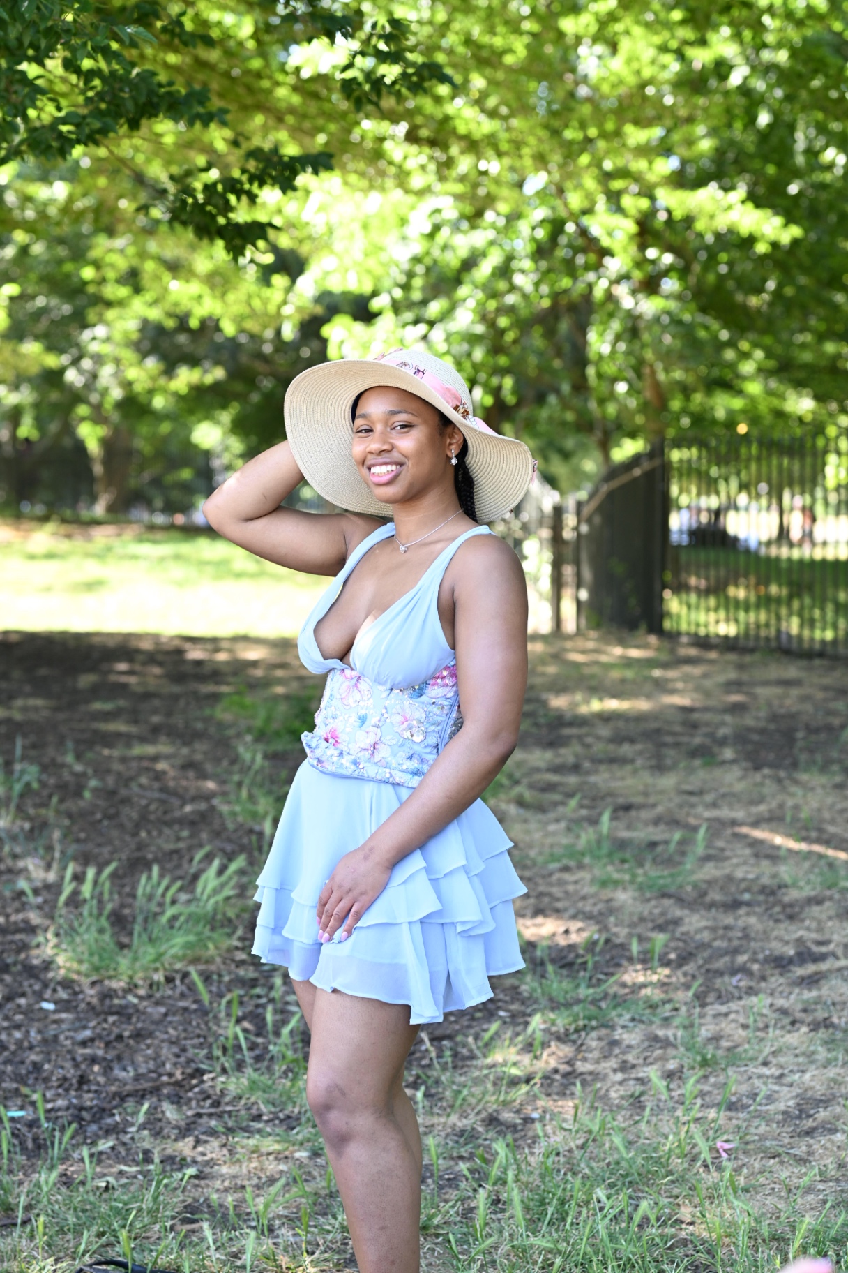 A member in a blue dress and straw hat posing in the park