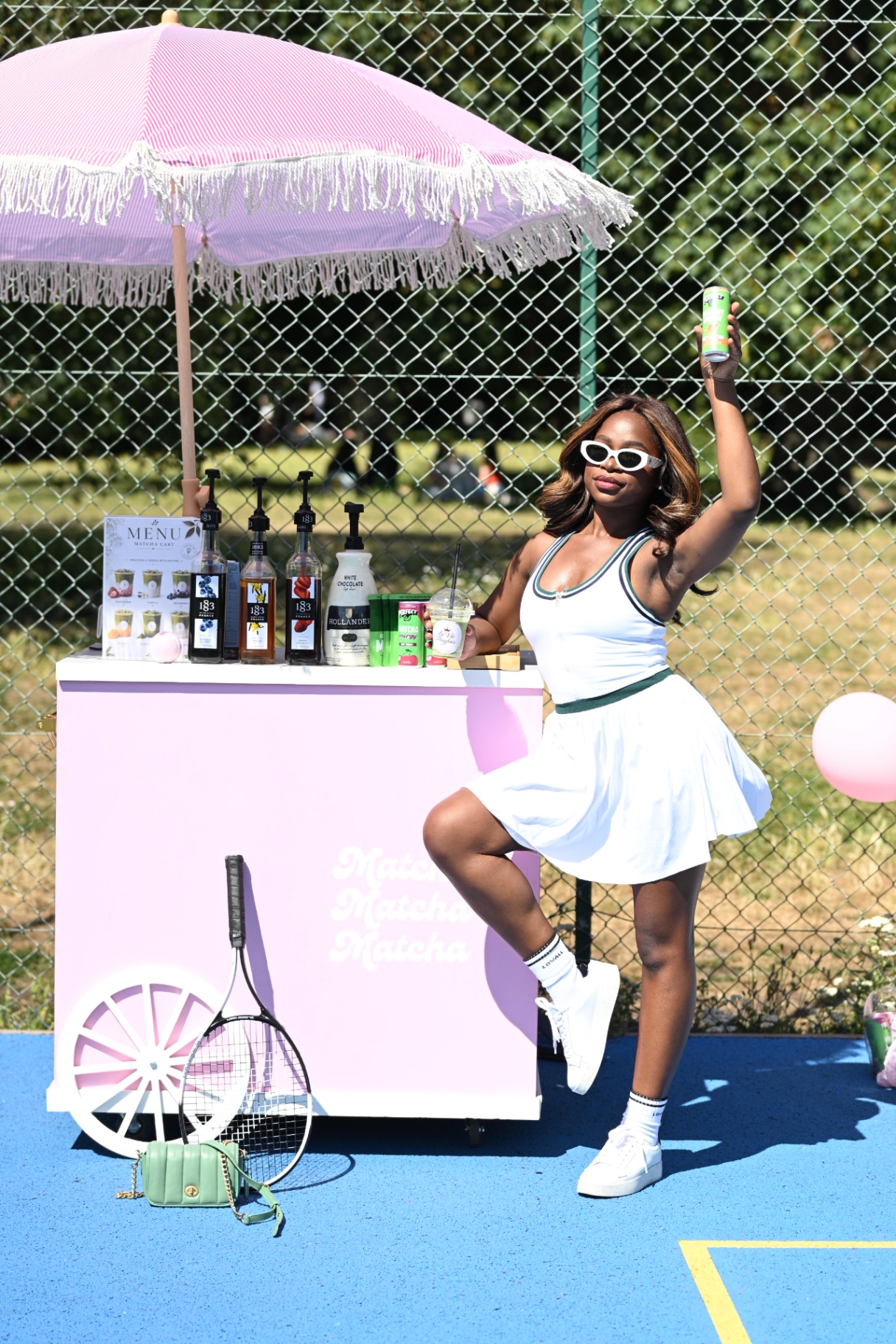 A member posing with a matcha can beside the pink matcha cart