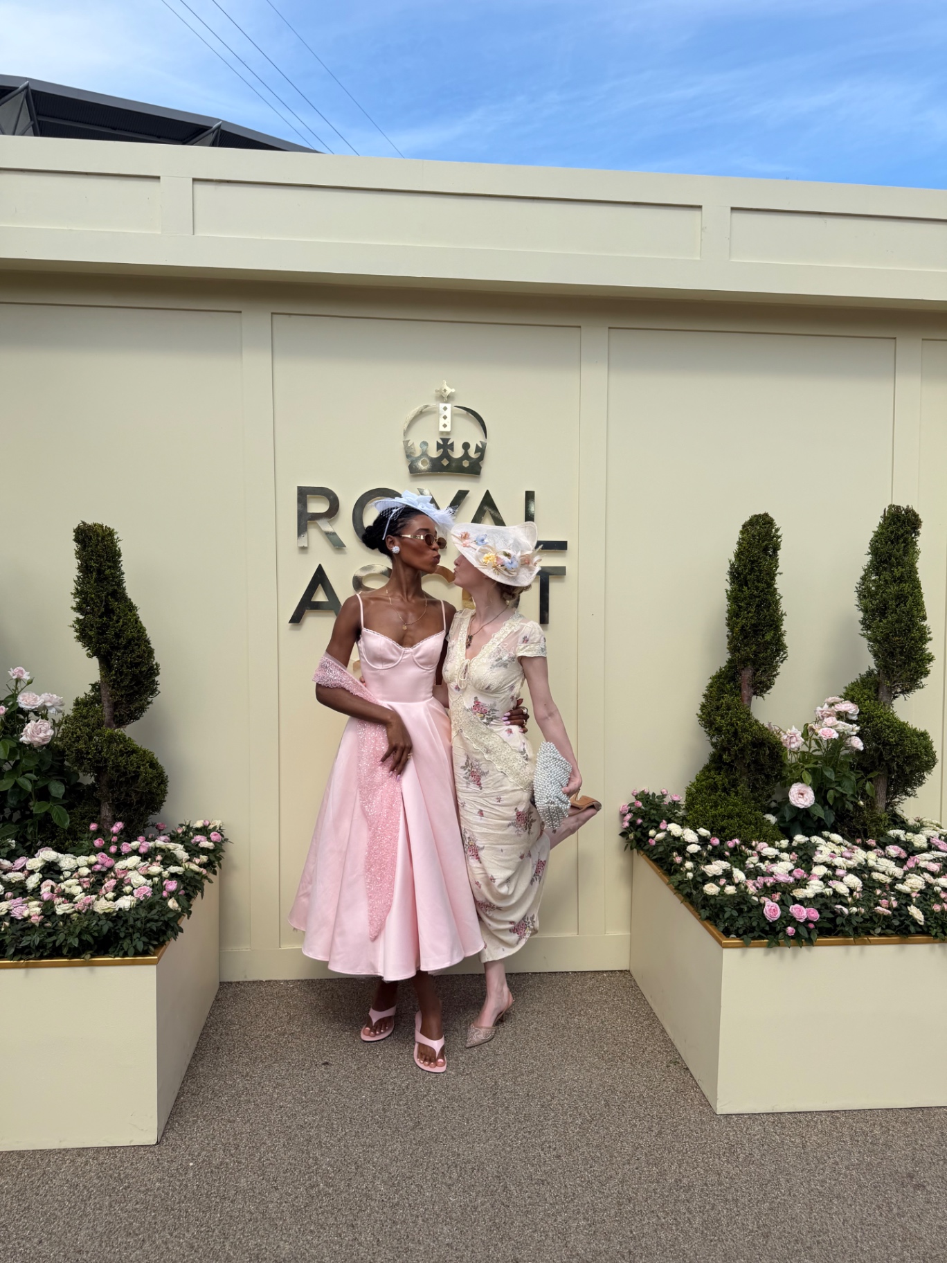 Two members in pink and floral dresses at the Royal Ascot sign