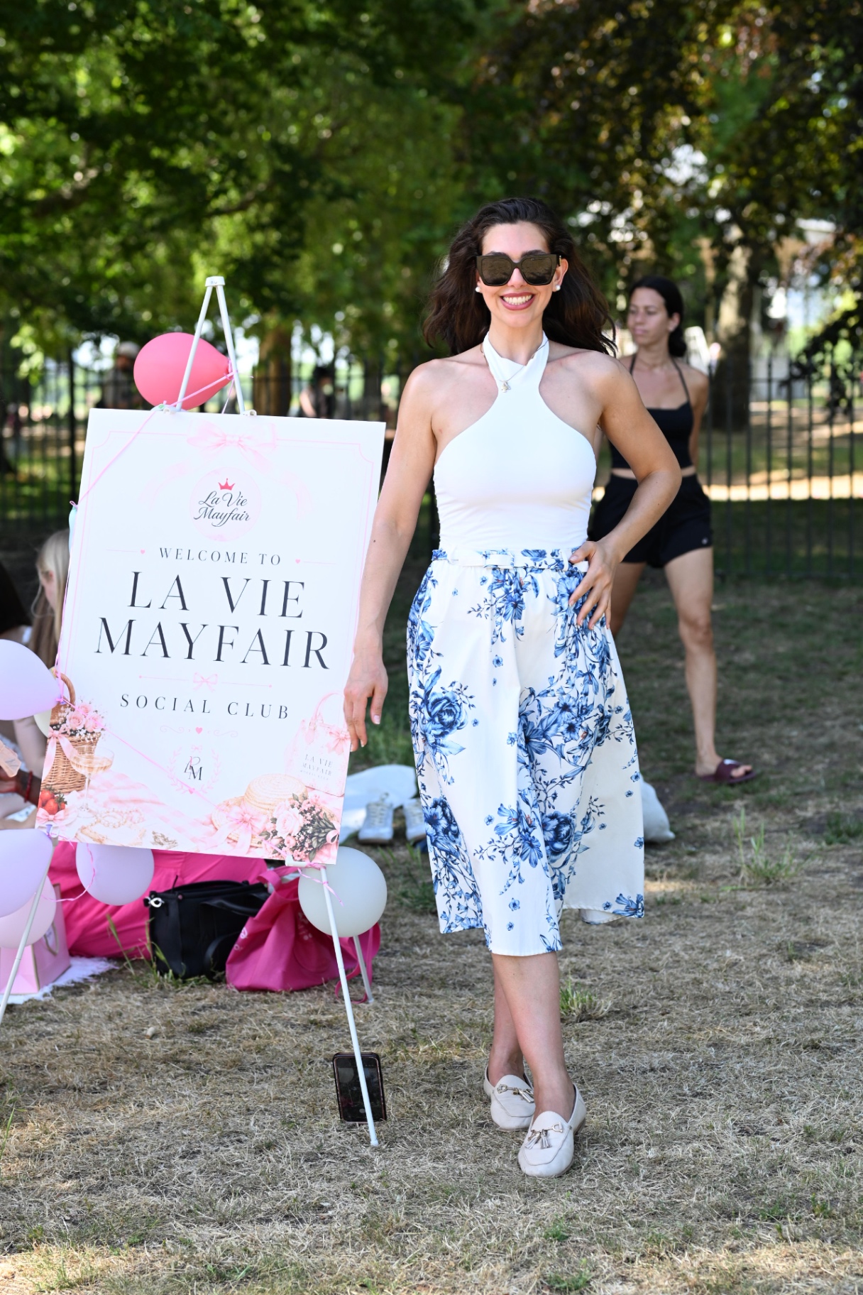 A member beside the Welcome to La Vie Mayfair Social Club sign at the picnic