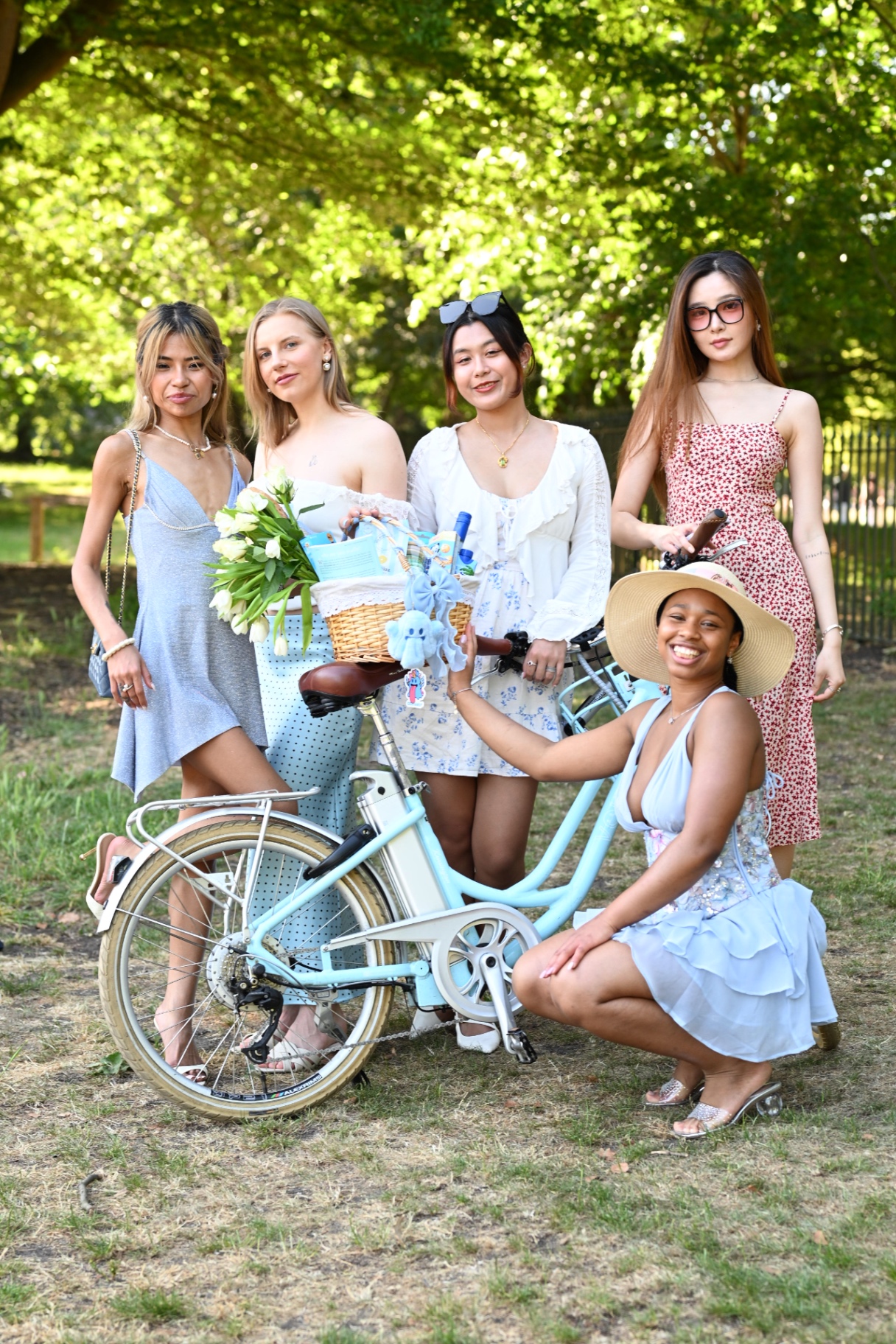 Members posing with a pale blue bicycle and picnic basket in the park