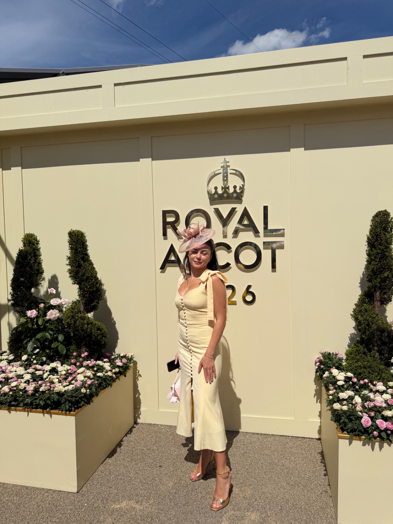 A member in a lemon yellow dress by the Royal Ascot 2026 sign
