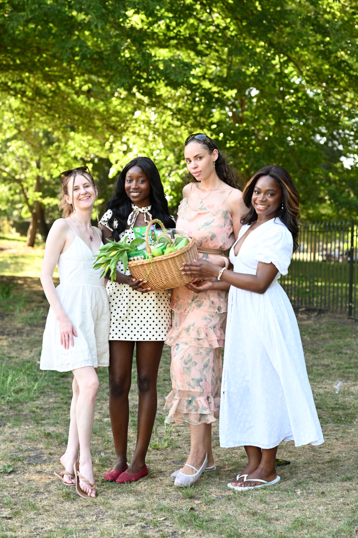 Members holding a green-themed picnic hamper under the trees