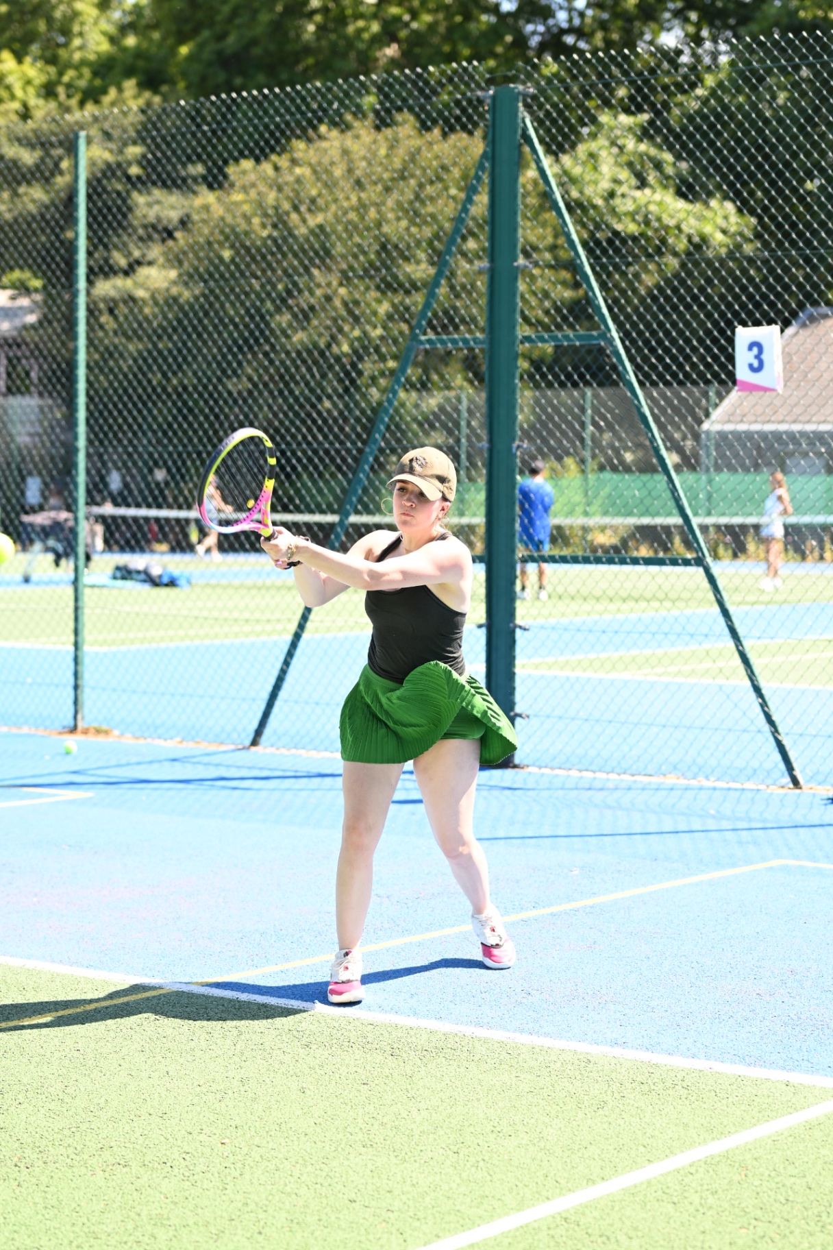 A member in a green tennis skirt hitting a backhand on court