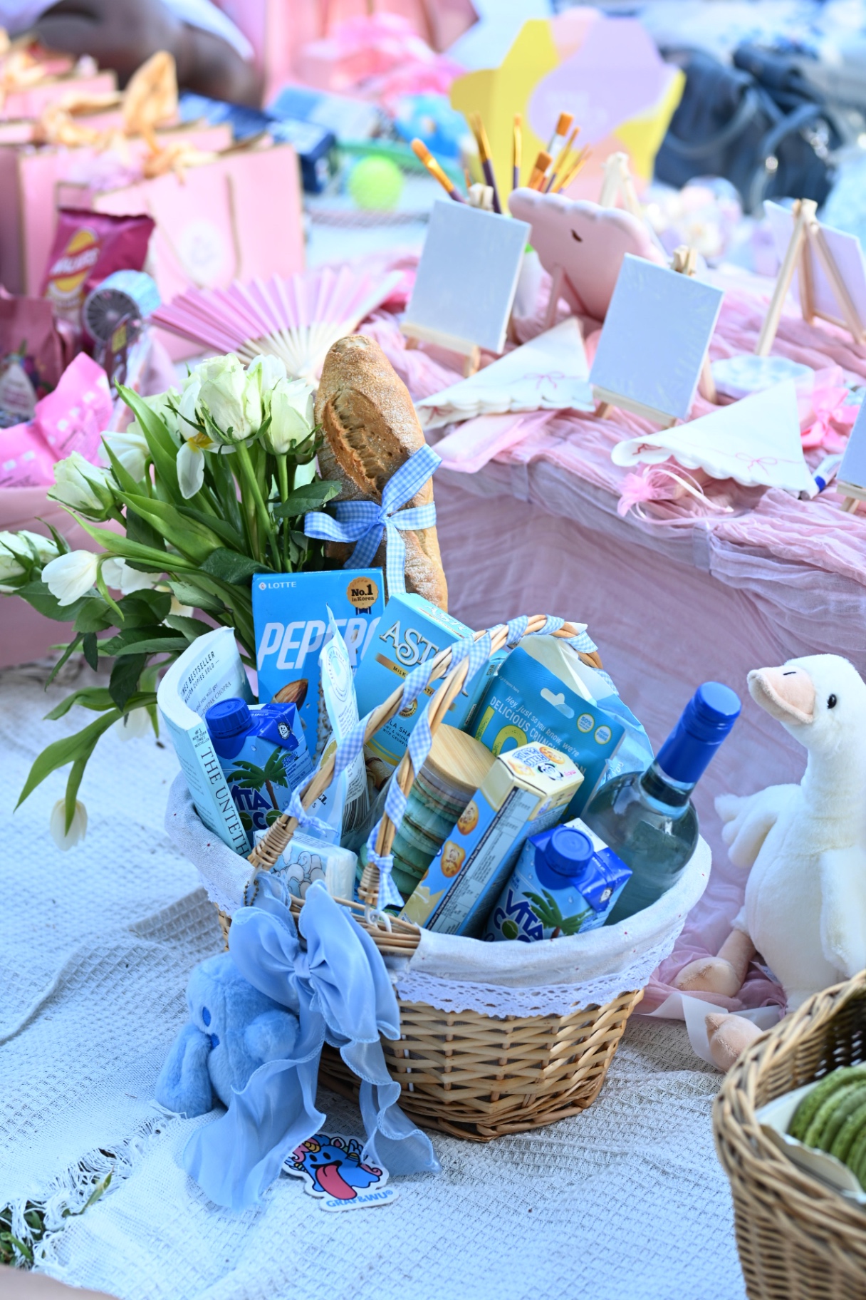 A blue-themed picnic hamper with flowers and painting easels behind