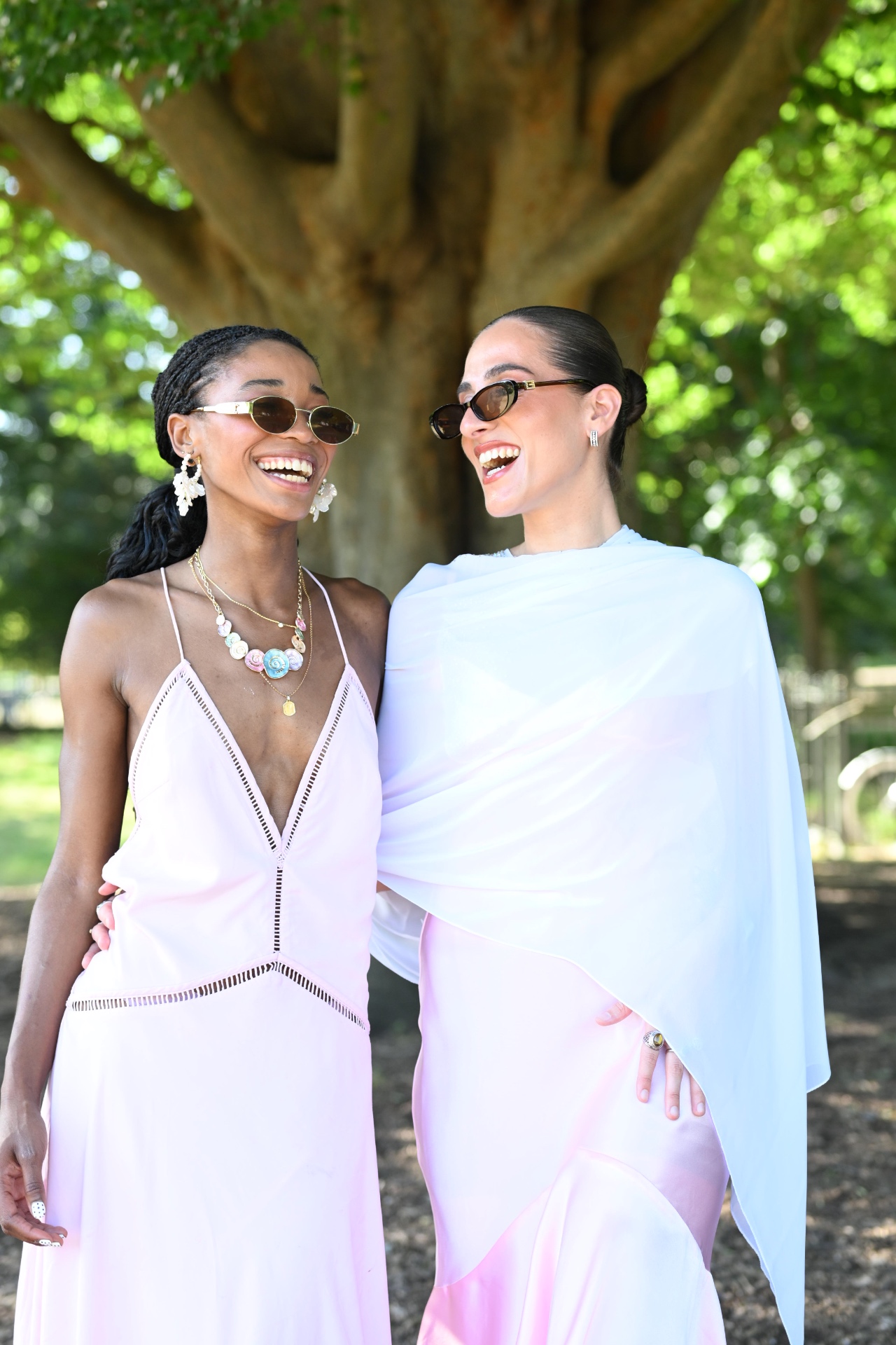 Two members laughing together in pastel dresses under a tree