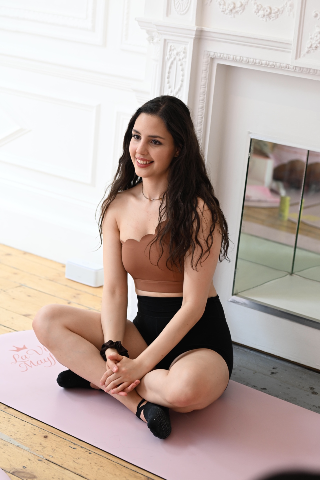 A member sitting cross-legged on a pink La Vie Mayfair mat