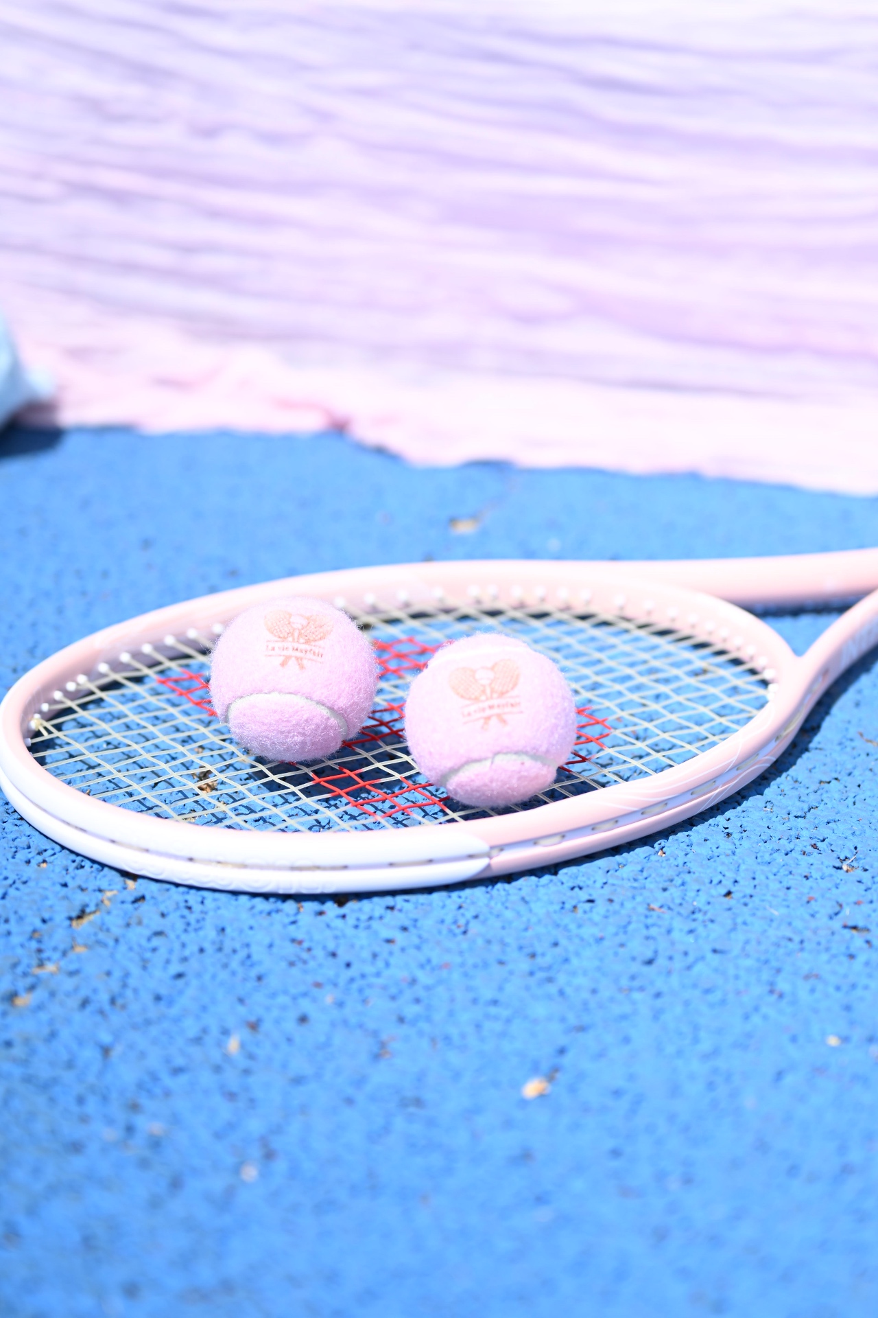 Pink La Vie Mayfair tennis balls resting on a pink racket on court