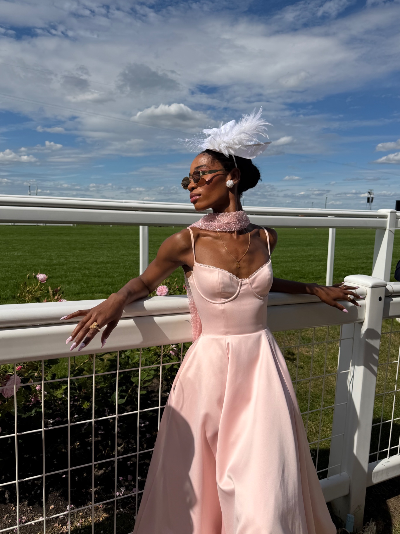 A member in a blush satin gown and feathered fascinator trackside