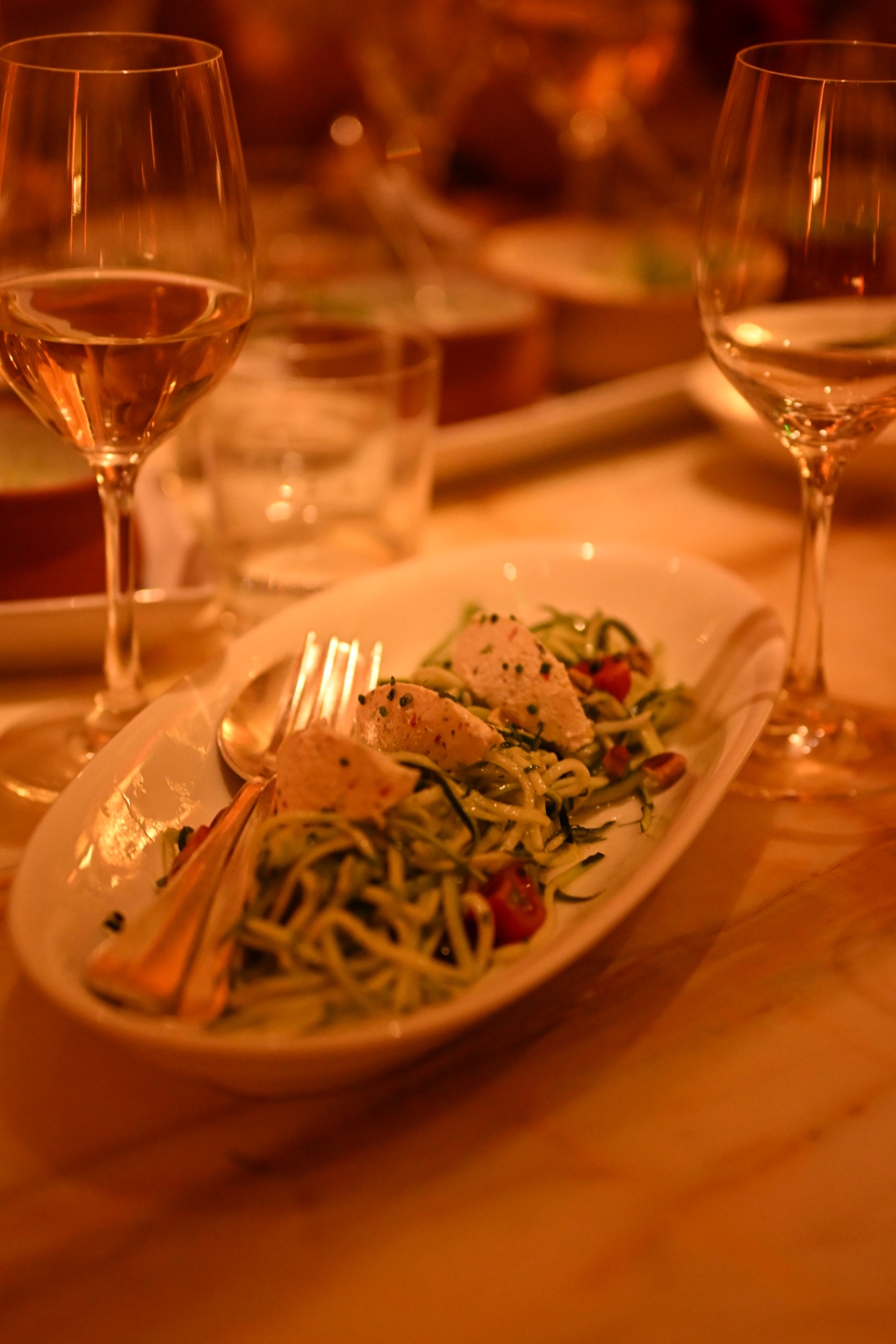 A courgette salad plated beside wine glasses at dinner