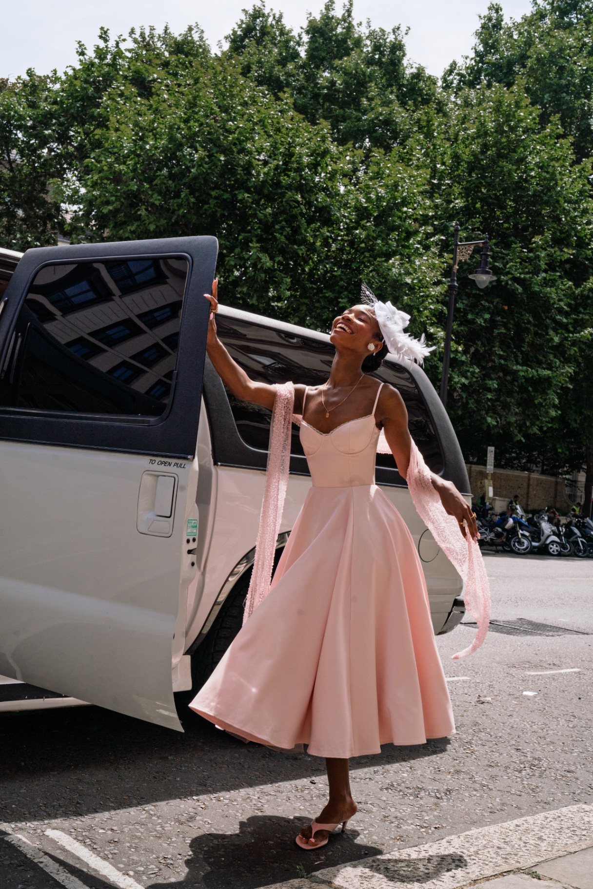 A member laughing in a pink gown by the limousine door