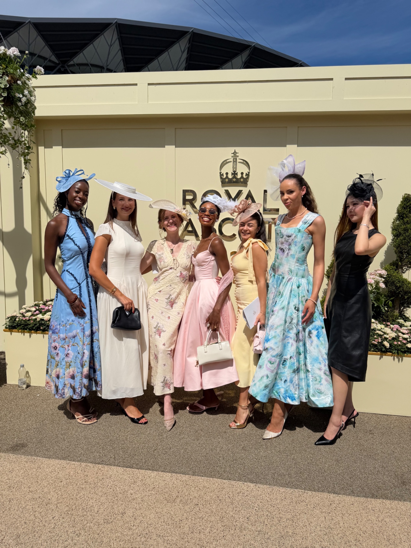 Members posing together in hats and gowns at the Royal Ascot entrance