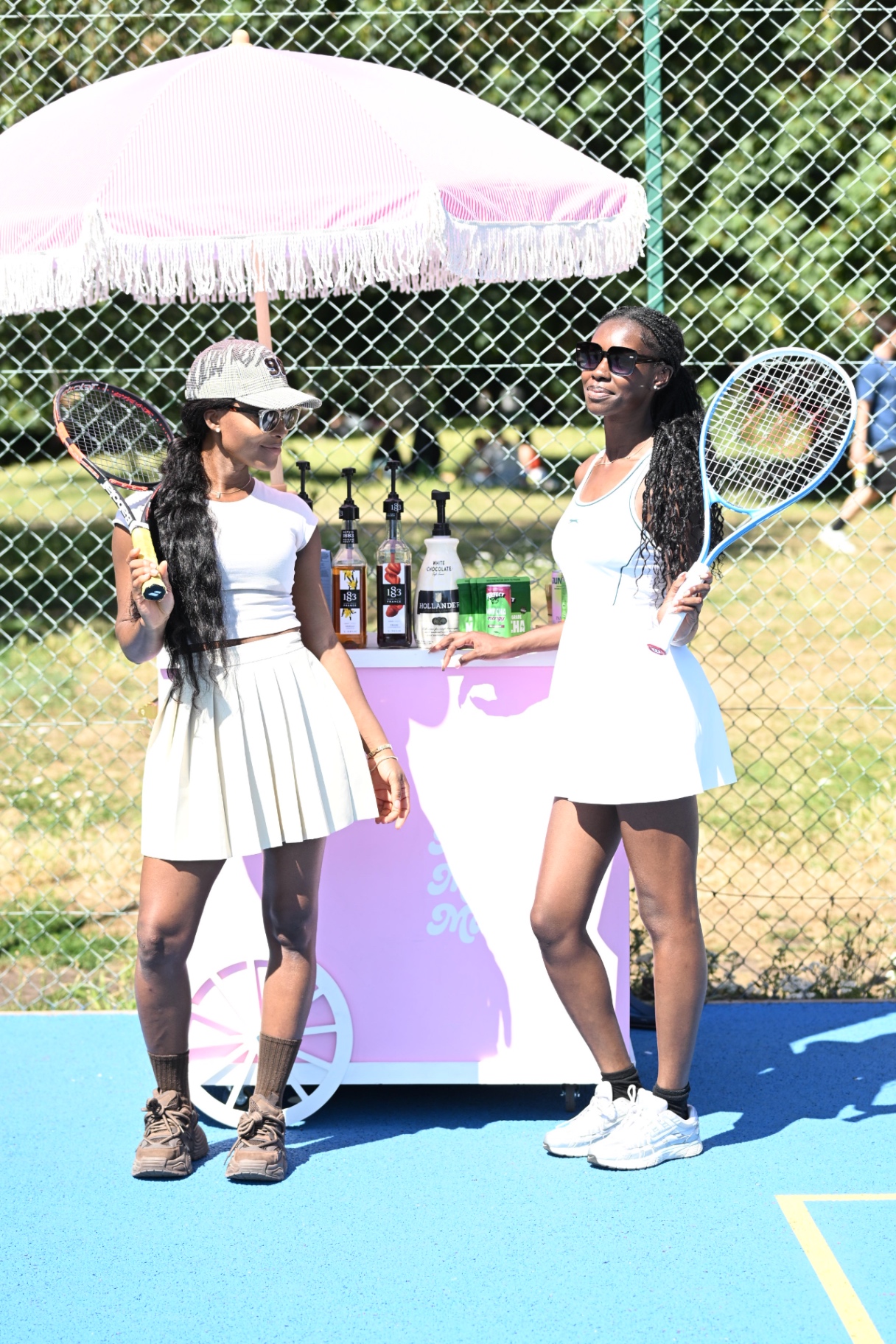 Two members in tennis whites posing with rackets at the matcha cart