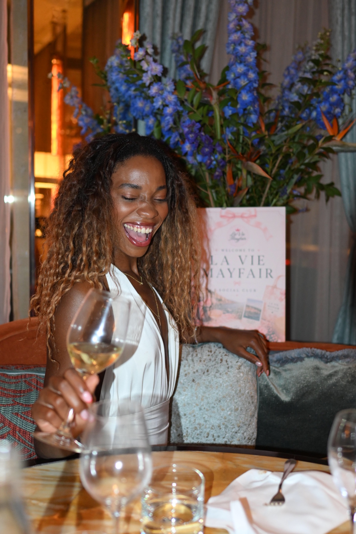A member laughing with a glass of wine beside the La Vie Mayfair welcome sign