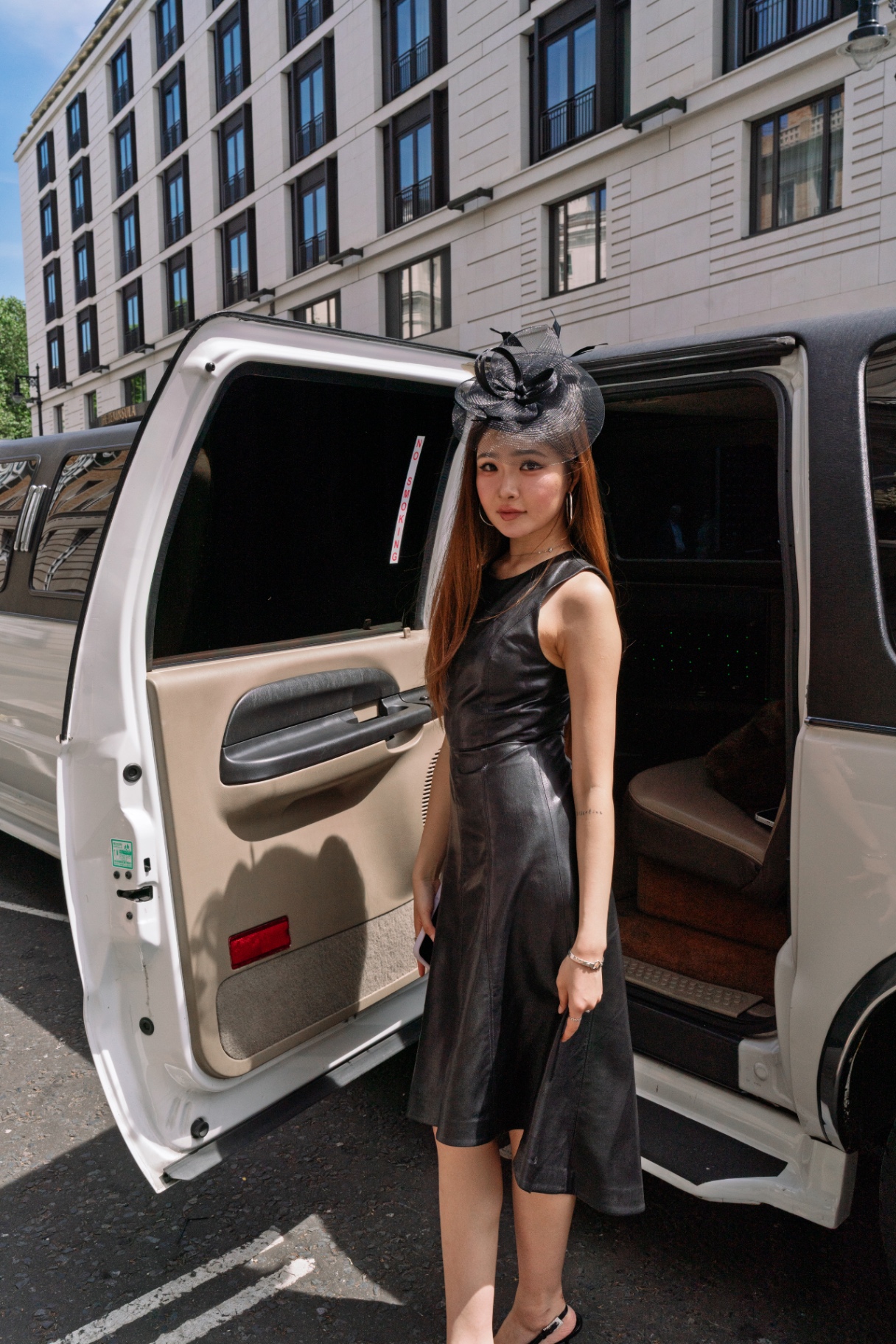 A member in a black dress and fascinator beside the limousine door in Mayfair